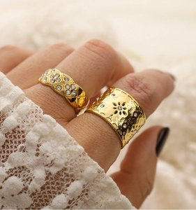 Dettaglio di anelli vintage placcati oro con incisioni floreali e strass su sfondo di pizzo