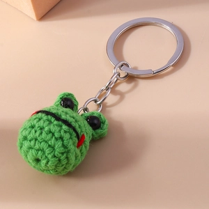 Macro detail of hand-knitted green frog keychain with silver metal ring and soft texture