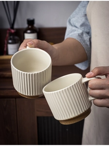 Detail of hand holding two off-white ceramic mugs with vertical striped texture and brown base