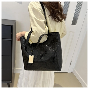 Detail view of the black crocodile pattern texture on a glossy faux leather tote bag