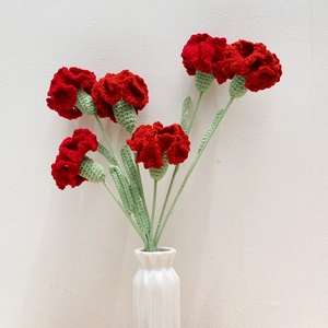 Close-up of six handmade red crochet carnations with green stems in a white ceramic vase
