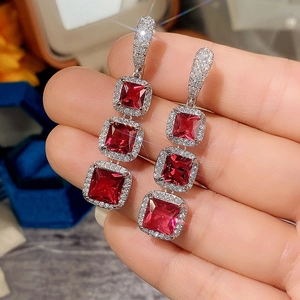 Close-up of sparkling silver drop earrings with three square red stones and cubic zirconia