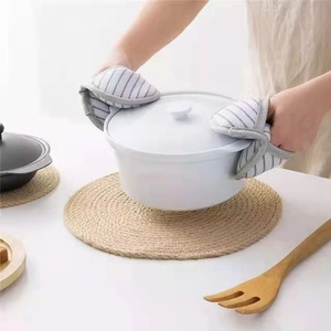 Gray striped cotton oven mitts lifting a white ceramic pot on a woven round placemat