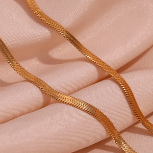Close-up of golden flat snake chain necklace on elegant pink pleated satin fabric