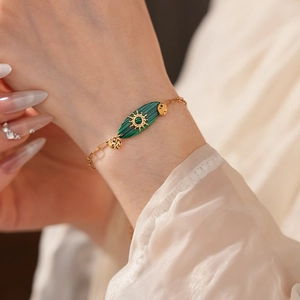 Détail d'un bracelet vintage doré avec pierre vert émeraude et motif rayon de soleil au poignet