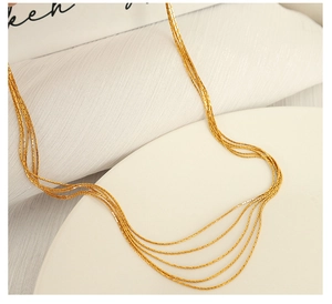 Detailed view of layered gold snake chains draped over a minimalist white display stand