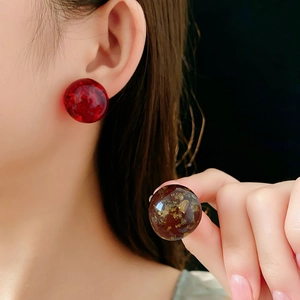 Close-up of amber resin stud earrings with gold foil and red cracked sphere detail