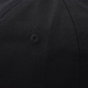 Gros plan sur l'œillet brodé et la texture en coton sergé de la casquette noire
