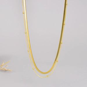 Minimalist double-layered gold snake chain necklace with small beads on a light grey background