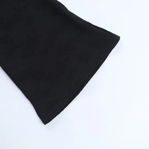 Détail du tissu jacquard noir montrant la texture florale et la coupe de manche évasée