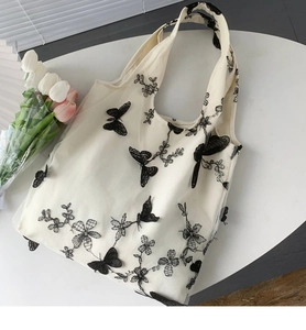 Dettaglio del ricamo a farfalla nera su borsa tote in pizzo a rete bianca