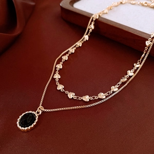 Close-up of double-layer gold heart chain and oval black stone pendant on silk fabric
