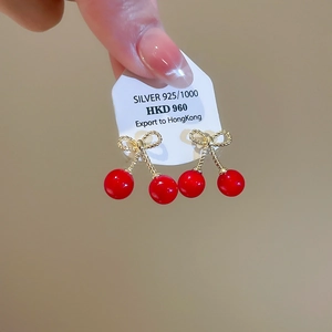 Macro detail of red resin cherry earrings with gold bow and 925 silver studs