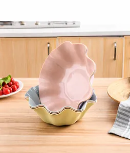 Stackable plastic fruit bowls with ruffled petal edges in pink and green on a wooden table