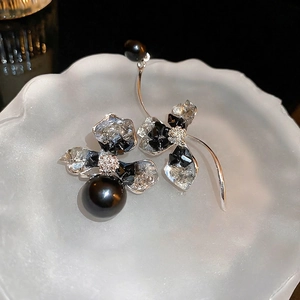 Asymmetrical crystal flower earrings featuring black pearls and silver metal on a black backdrop