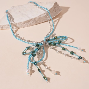 Detail of beaded bow necklace with blue crystals and long tassels on a stone display