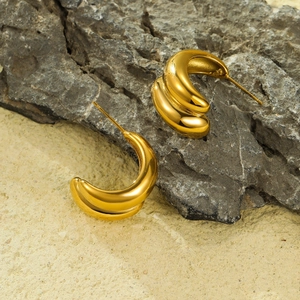 Detail of 18K gold-plated double-tube C-shape hoop earrings on a textured stone surface