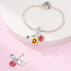 Macro detail of bread pendant and silver snake chain bracelet with vibrant enamel charms