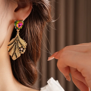 Close-up of vintage golden leaf earrings with heart gemstone and pearl flower on model