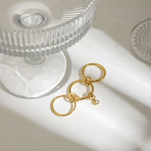 Détail de bagues superposées en acier doré avec un petit pendentif rond en zircon