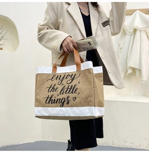 Detail of linen tote bag with 'Enjoy the little things' print and leather straps