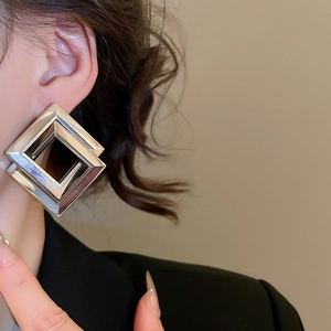 Macro shot of silver diamond-shaped layered earrings worn by a model in a black blazer