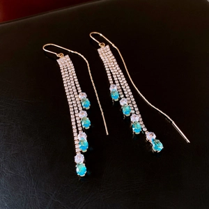 Macro shot of gold tassel earrings with zircon and teardrop-shaped teal gemstones