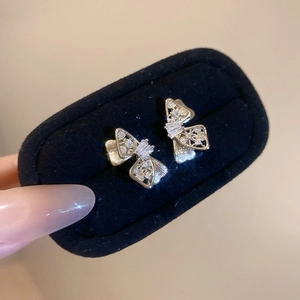 Close-up of golden bow-shaped stud earrings with zircons on a black velvet display