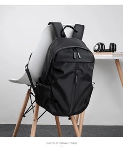 Zaino porta PC nero minimalista appeso a una sedia bianca con cuffie sullo sfondo