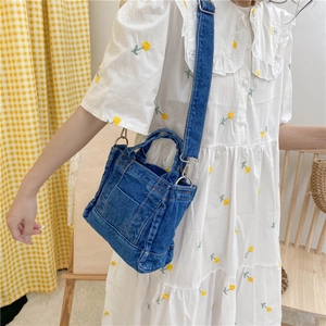 Detail view of a blue denim tote bag with a long strap worn by a model in a white dress