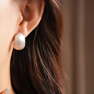 Detail of matte silver C-shape earring with brushed metal texture on female model