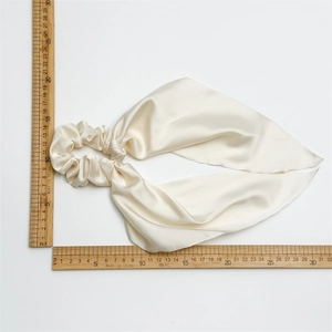 Detailed view of cream satin scrunchie with long ribbons measured by a wooden ruler