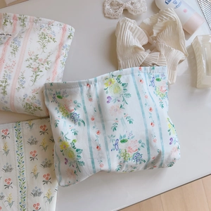 Flat lay of floral cotton cosmetic bags with hair accessories and skincare on white desk