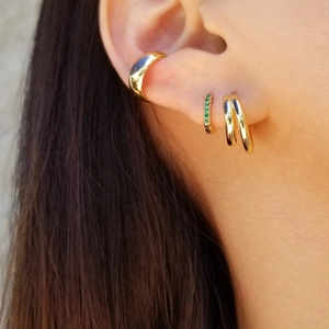 Close-up of stacked gold hoop earrings with green zircon inlay worn on a model's ear