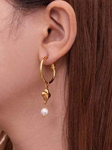 Nahaufnahme eleganter goldener Blumenohrringe mit weißem Perlenanhänger am Model