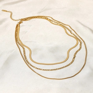 Detailed view of layered 18K gold-plated snake, Figaro, and square chain on white silk