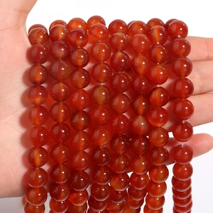 Polished natural red agate round beads for DIY jewelry making held in hand on white background