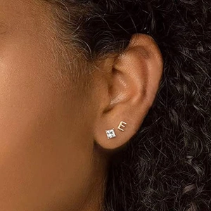 Detailed view of model wearing gold letter E and square crystal stud earrings set