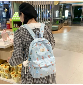 Detail view of light blue strawberry canvas backpack with plush charm and heart patterns