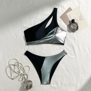 Detailed flat lay of silver metallic and black one-shoulder bikini with luxury accessories