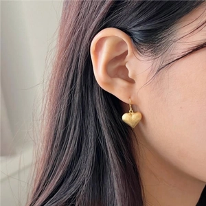 Close-up of elegant gold heart-shaped earrings with matte finish worn by a model