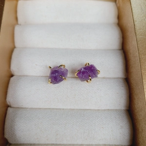 Elegant four-prong purple raw amethyst stud earrings with gold finish on velvet box