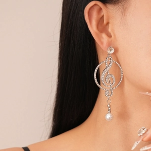 Close-up of music note earrings with sparkling crystals and a white pearl drop