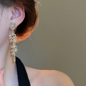 Vue détaillée de boucles d'oreilles pendantes dorées avec motifs feuilles et strass