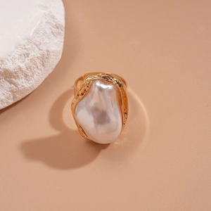 Gros plan d'une bague vague dorée avec une perle baroque irrégulière sur fond de pierre
