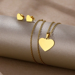 Polished gold heart necklace and earrings set displayed on elegant beige fabric surface