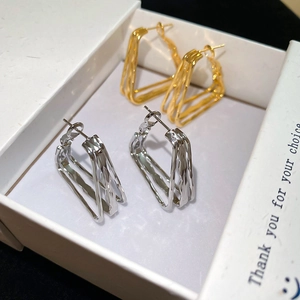 Macro shot of 18k gold and silver geometric twisted earrings inside a white gift box