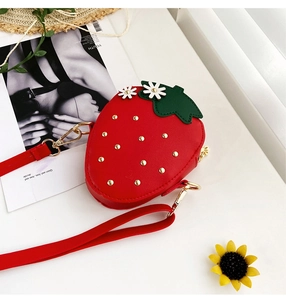 Macro detail of red strawberry shaped crossbody bag with green leaf and flower accents
