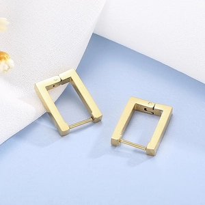 Macro shot of minimalist gold geometric rectangular hoop earrings on textured fabric