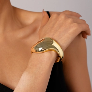 Hochglanzpoliertes, goldfarbenes Manschettenarmband im organischen Design am Handgelenk